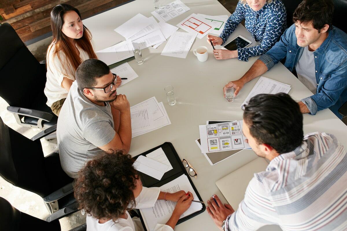 Group of professionals in a meeting discussing strategies around a table with documents and coffee.