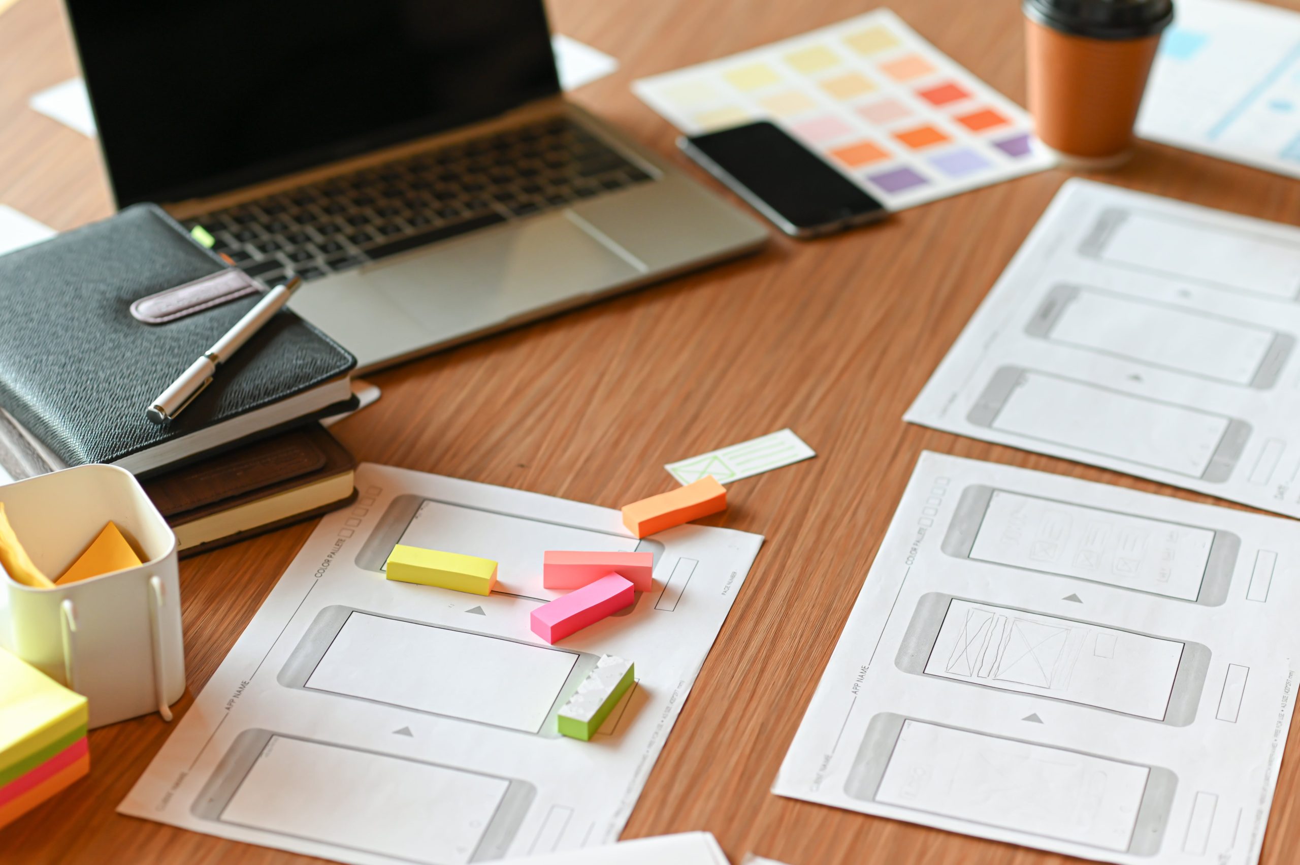 Designer's desk with laptop, notebooks, color charts, and smartphone, showcasing creative workspace essentials.