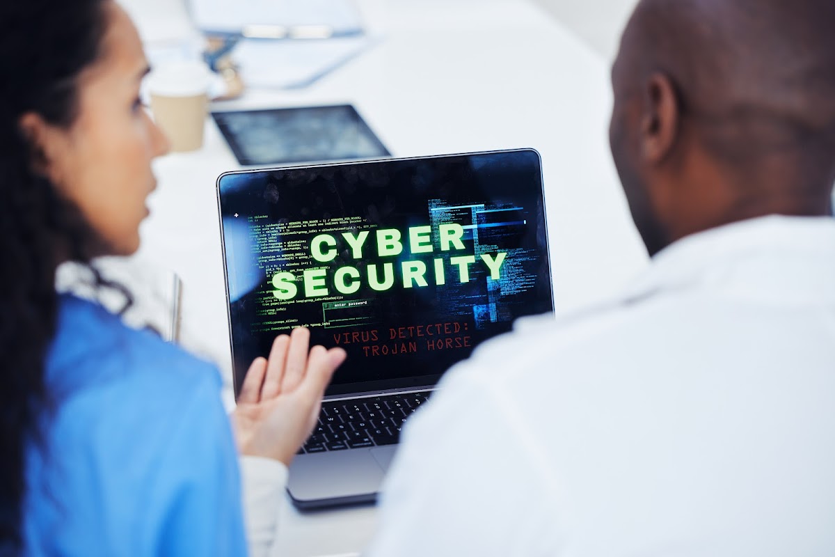 Two professionals engaged in a discussion while looking at a laptop screen displaying a cybersecurity warning, with the text 