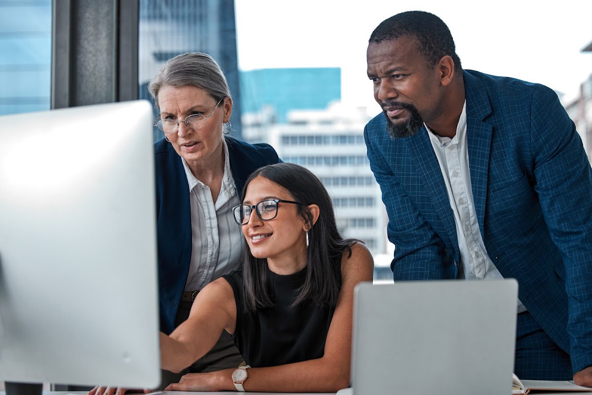 A diverse group of business people collaborate in an office, focusing on a computer screen for teamwork.