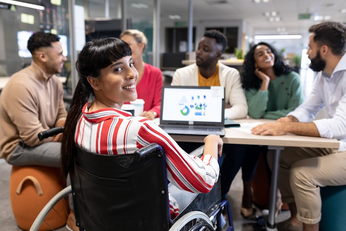 Businesswoman in a wheelchair smiling at a meeting in a modern office setting.