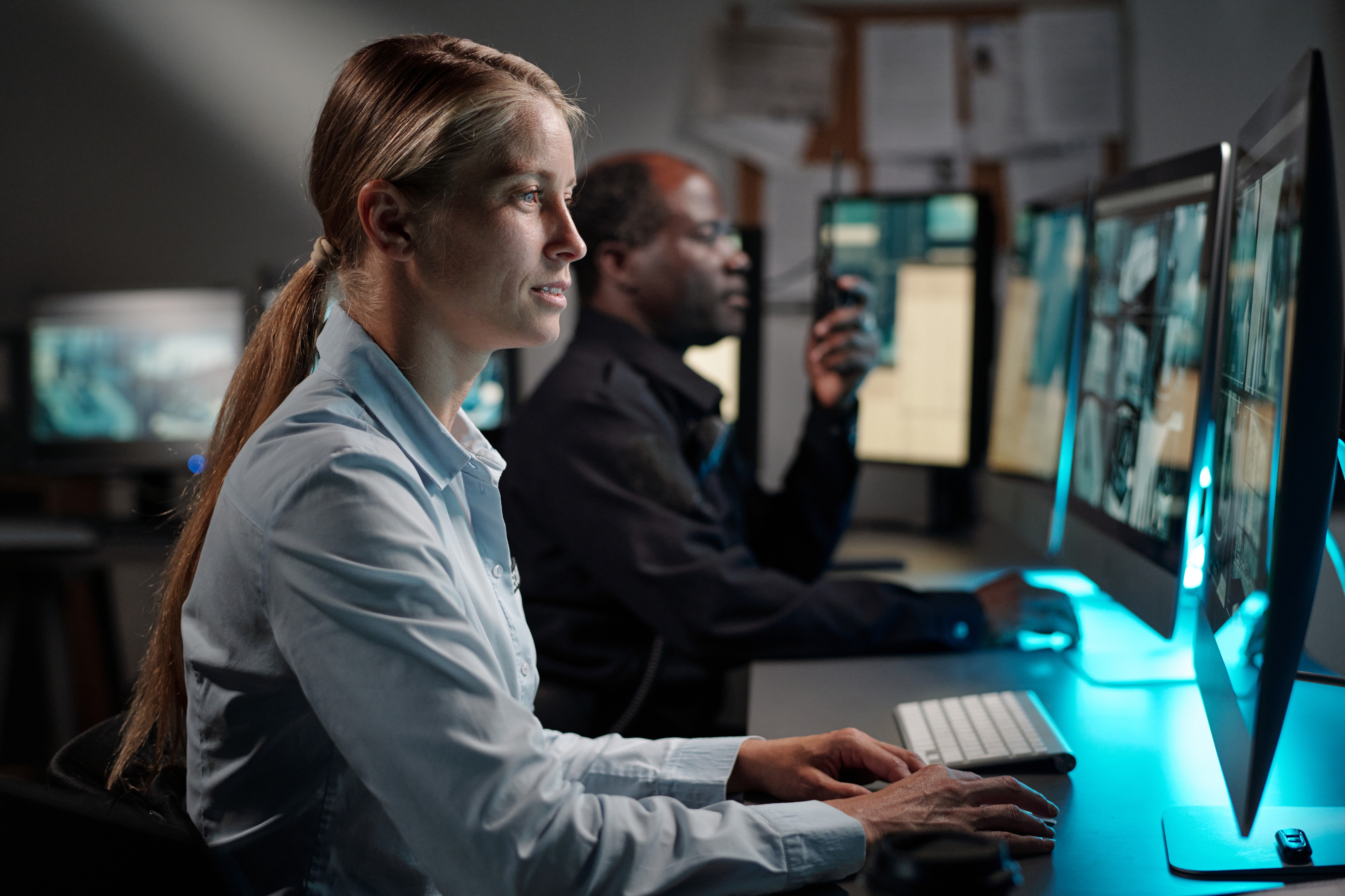 Professional team working at computer stations with multiple screens, focused on data analysis in a dimly lit office.